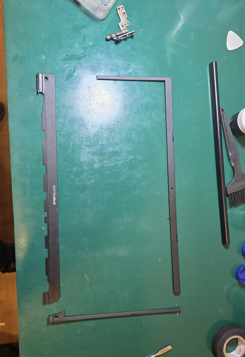 Moldura da tela do Asus Vivobook X513EA quebrada em partes, ao lado das dobradiças removidas