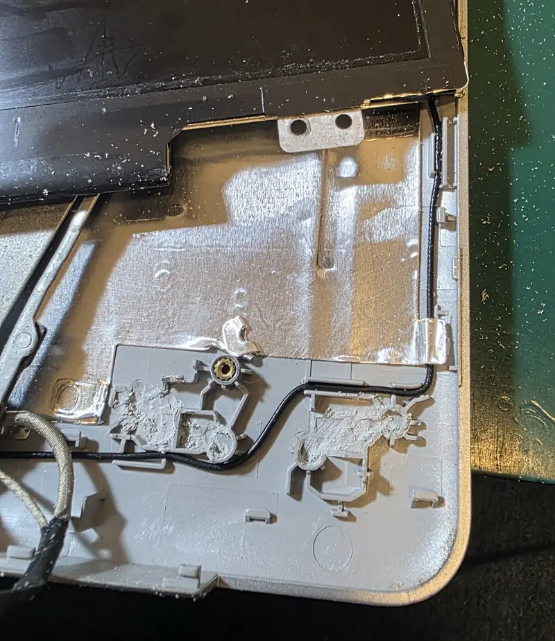 Tampa da tela do Dell Inspiron 5770 aberta mostrando as fixações plásticas da dobradiça quebradas